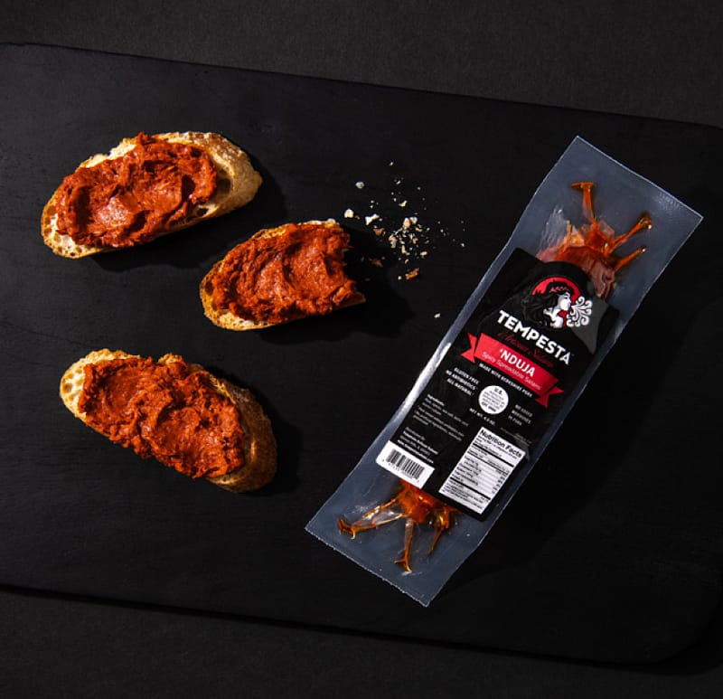 Tempesta 'nduja spread on crusty bread next to a package of spicy spreadable Calabrian salami